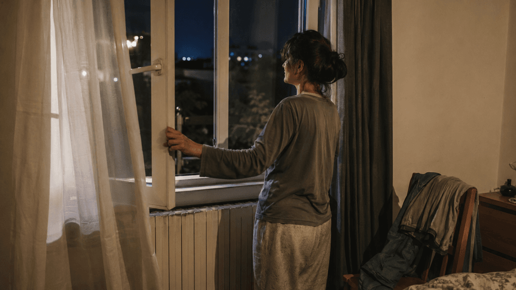 Frau öffnet am Abend ein Fenster in einer einfachen Wohnung