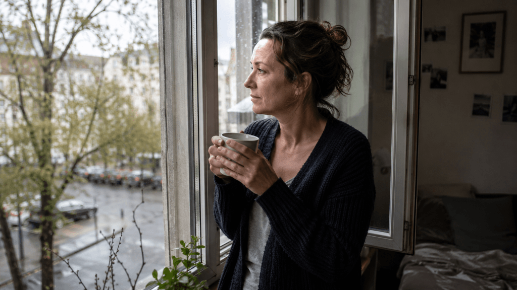 Frau bei einer kreativen Auszeit am Fenster nach einem Regentag