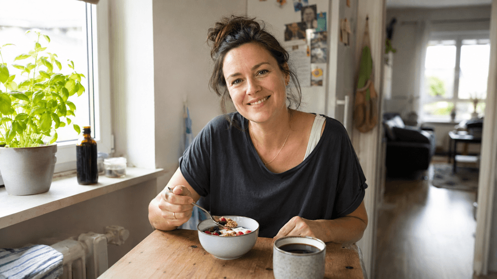 Frau frühstückt entspannt Joghurt mit Obst und Kaffee