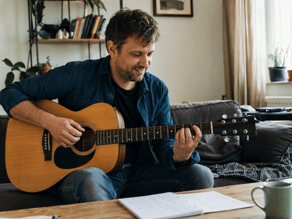 Mann sitzt zu Hause auf dem Sofa und übt entspannt Gitarre als neues Hobby
