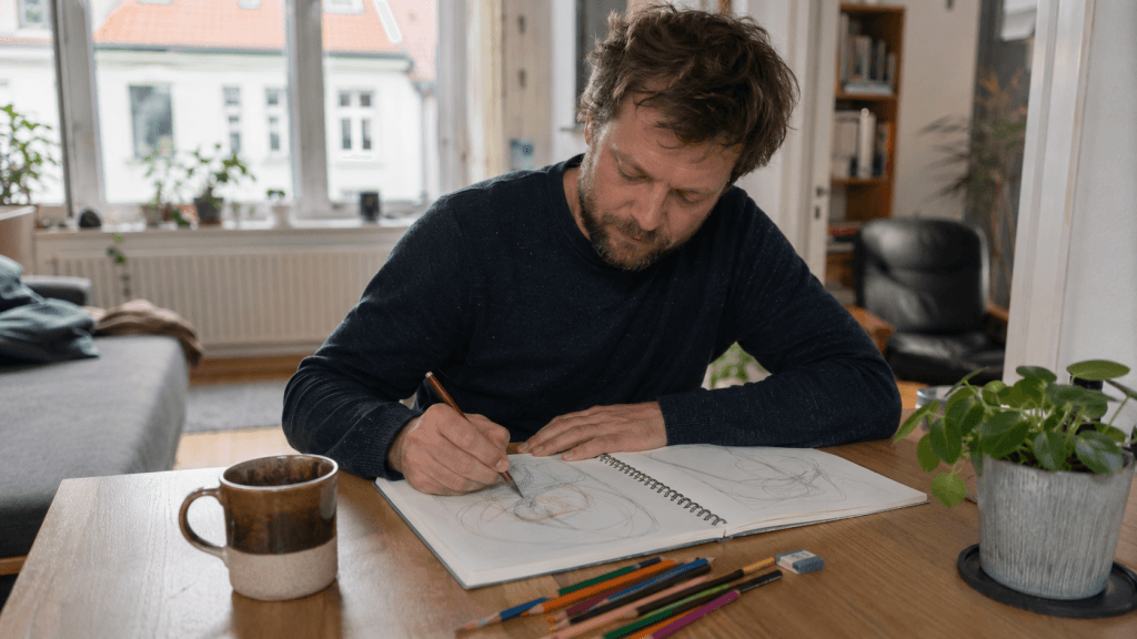 Mann probiert zu Hause ein kreatives Hobby mit Skizzenbuch, Buntstiften und Kaffee aus