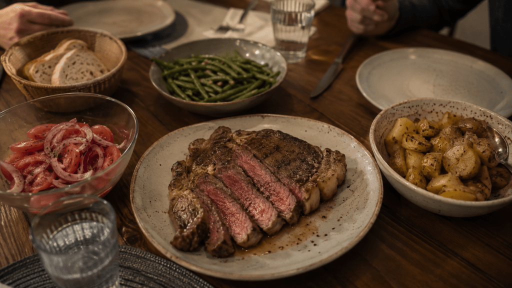 Geschnittenes Rib-Eye-Steak auf dem Tisch mit einfachen Beilagen