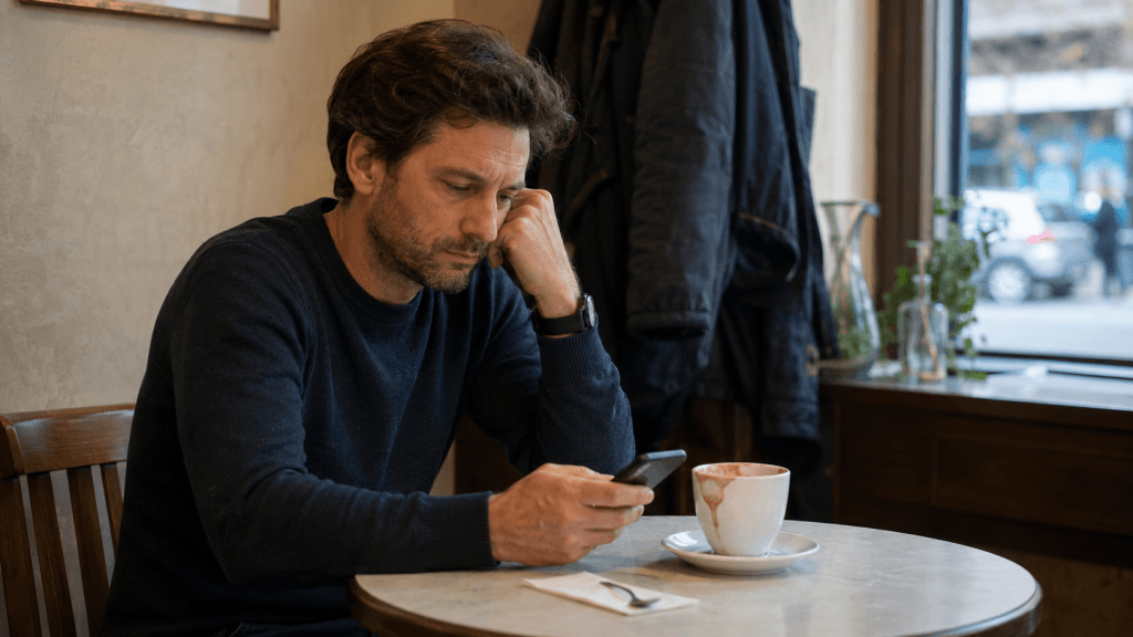 Nachdenklicher Mann im Café mit Kaffee und Smartphone