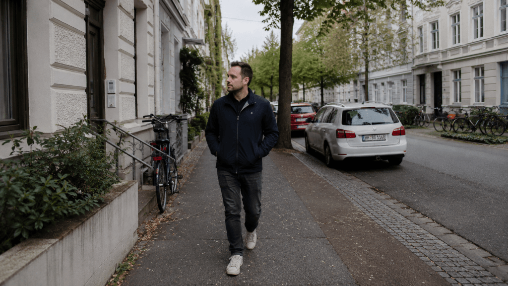 Mann geht allein auf einer ruhigen deutschen Wohnstraße mit Bäumen, Fahrrädern und Altbauten