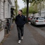 Mann geht allein auf einer ruhigen deutschen Wohnstraße mit Bäumen, Fahrrädern und Altbauten