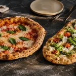 Unterschied zwischen Pizza und Pinsa mit runder Pizza und ovaler Pinsa auf dunklem Steintisch