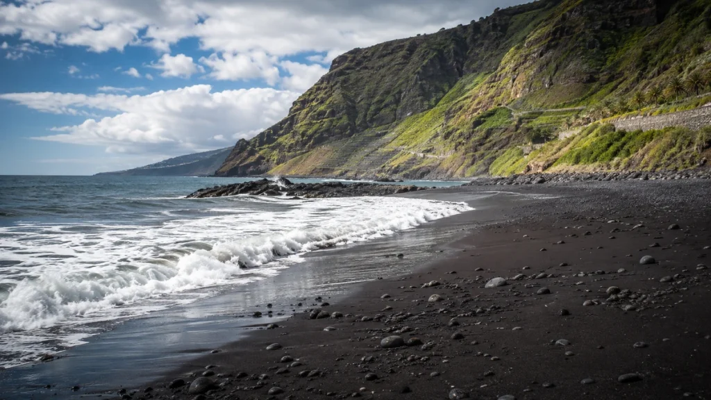 Schwarzer Sandstrand im Norden Teneriffas mit Atlantikwellen und grünen Klippen